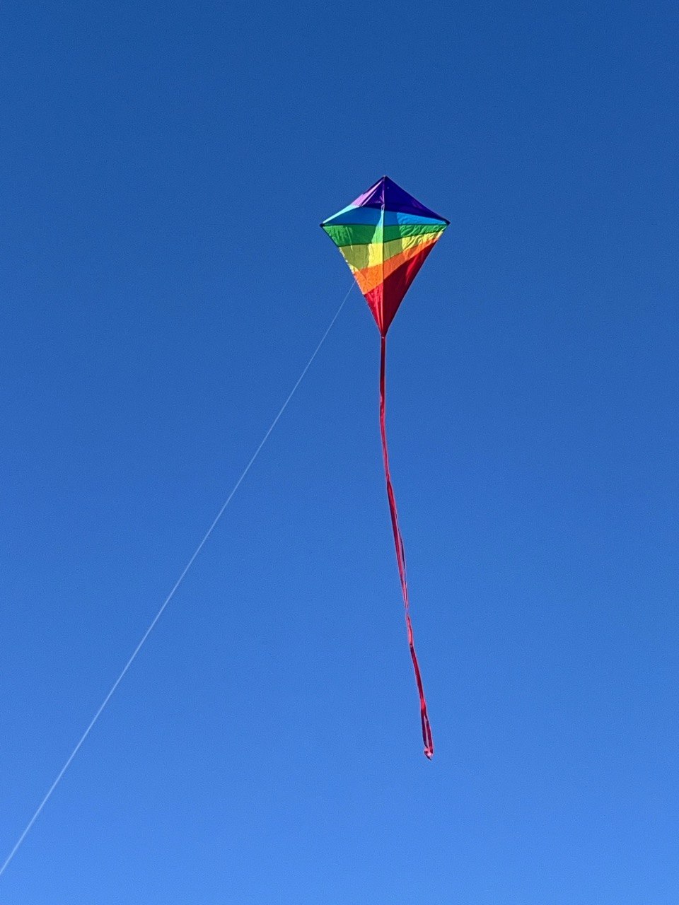 A bright rainbow-coloured kite soaring high against a clear blue sky