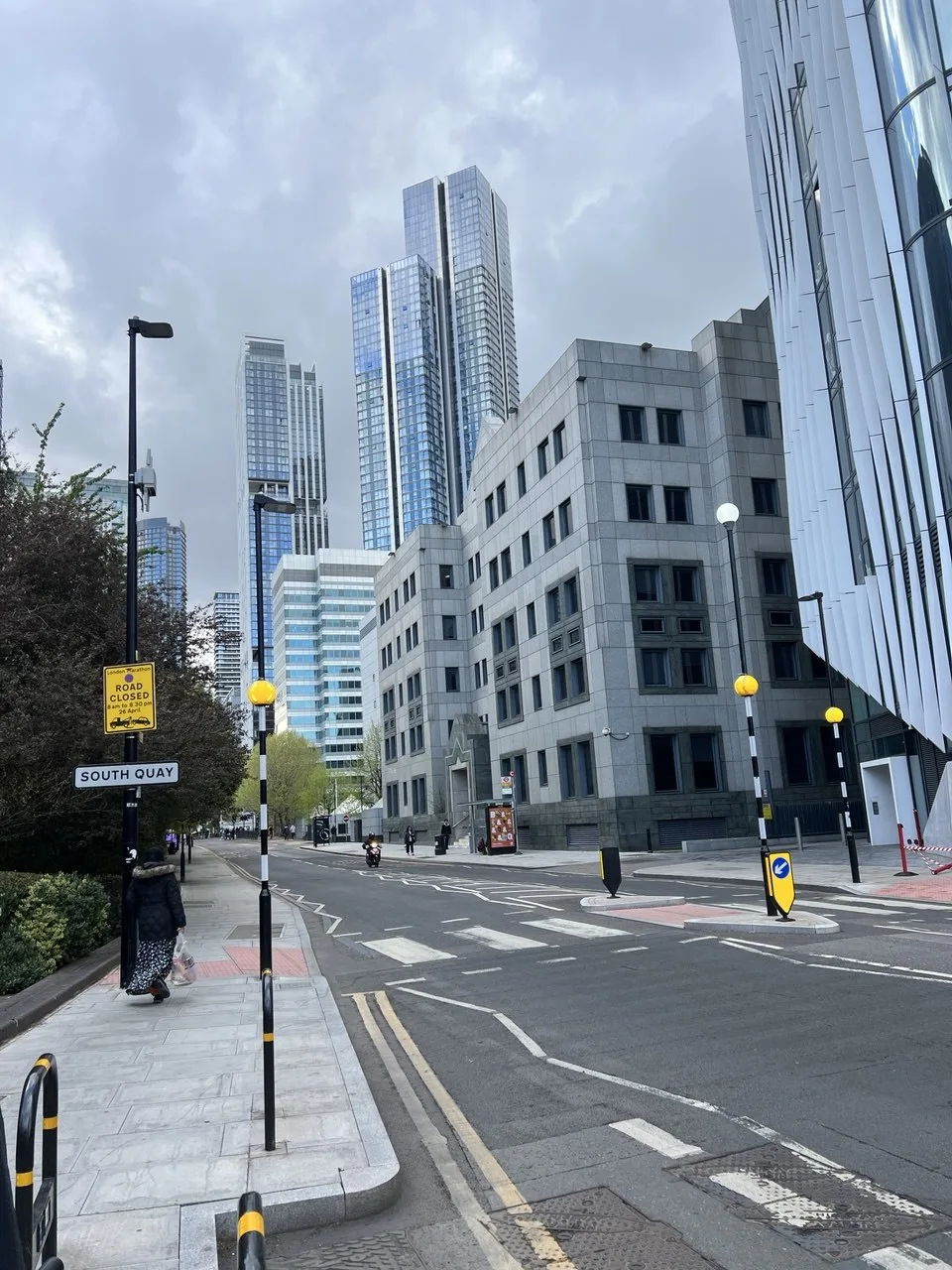 A quiet city street lined with tall glass towers under a soft grey sky
