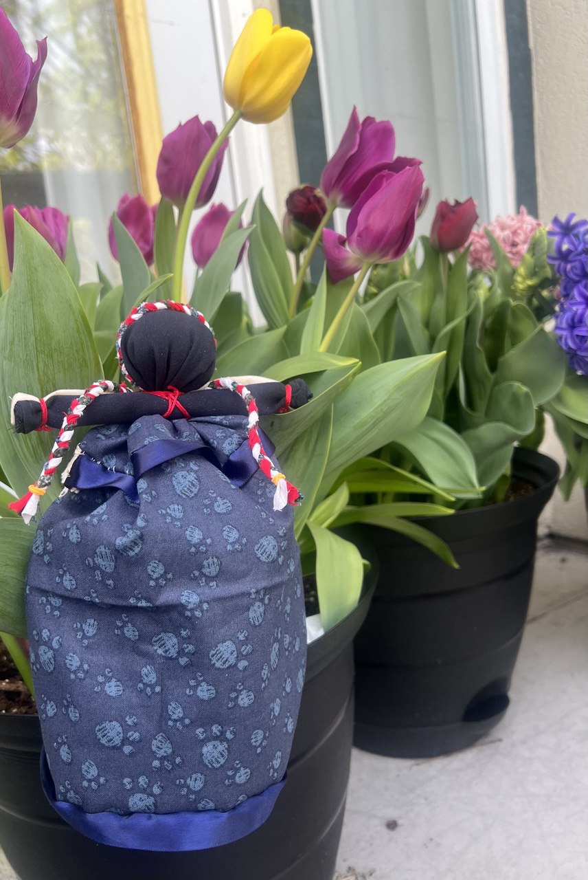 A double-sided handmade doll placed beside a vase of spring flowers